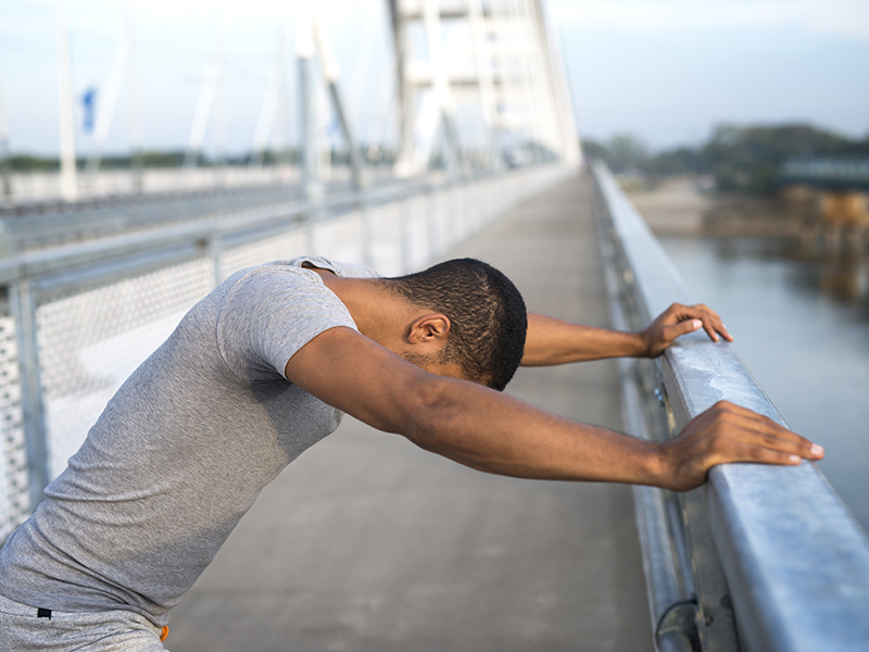 Un homme qui s'étire les bras à la rambarde d'un pont pendant sa séance de sport